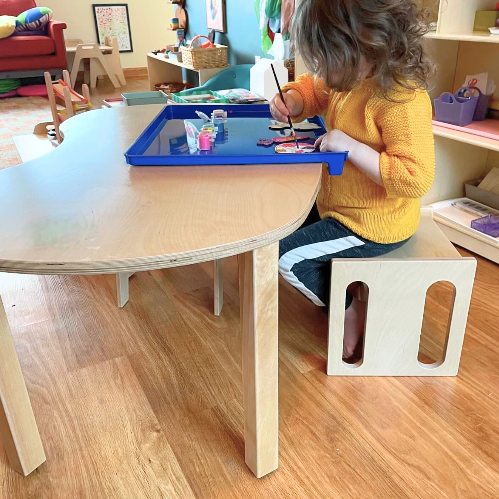 Child sitting at a table with a blue tray, engaged in an activity in a classroom setting.