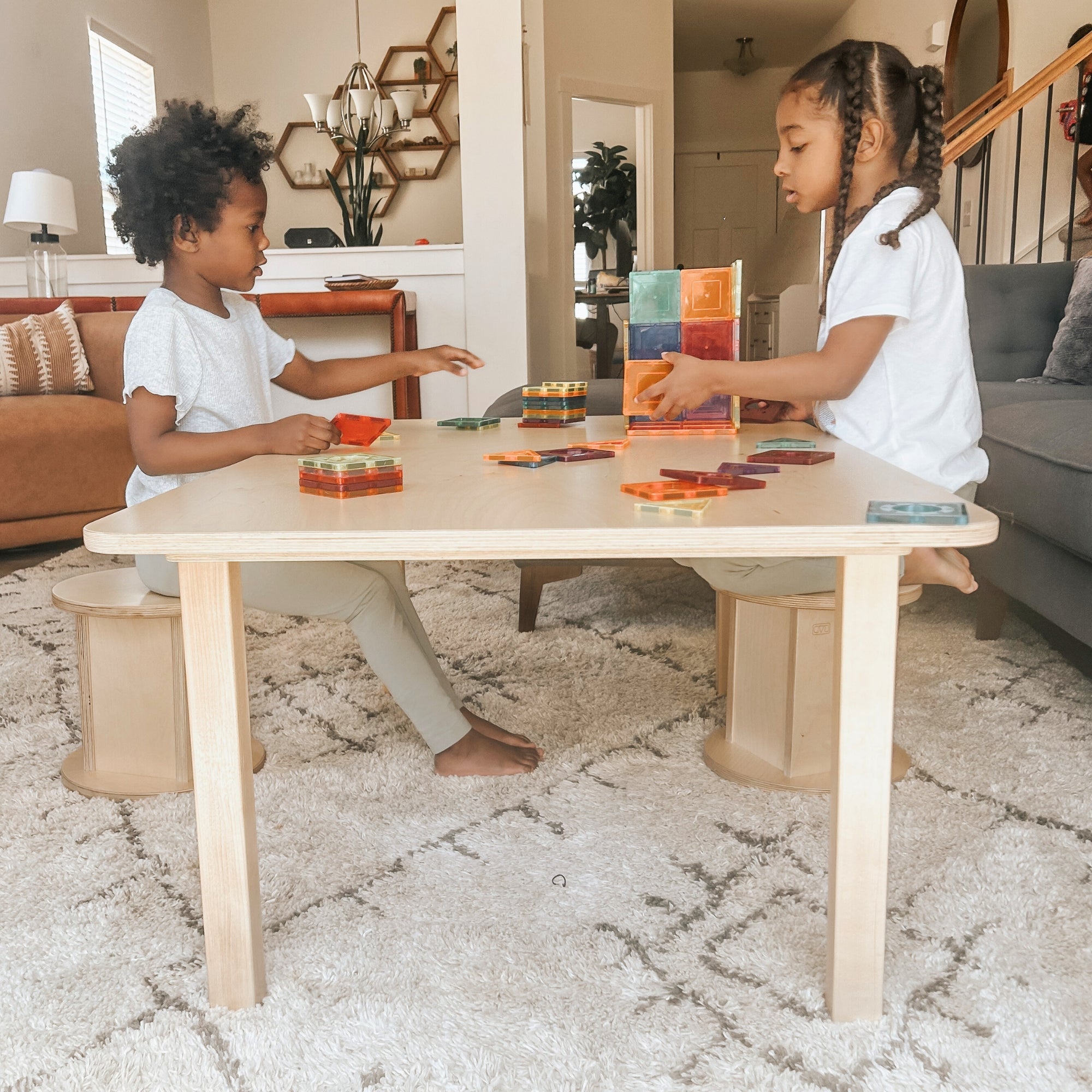 Two children playing with colorful blocks at a wooden table in a living room.