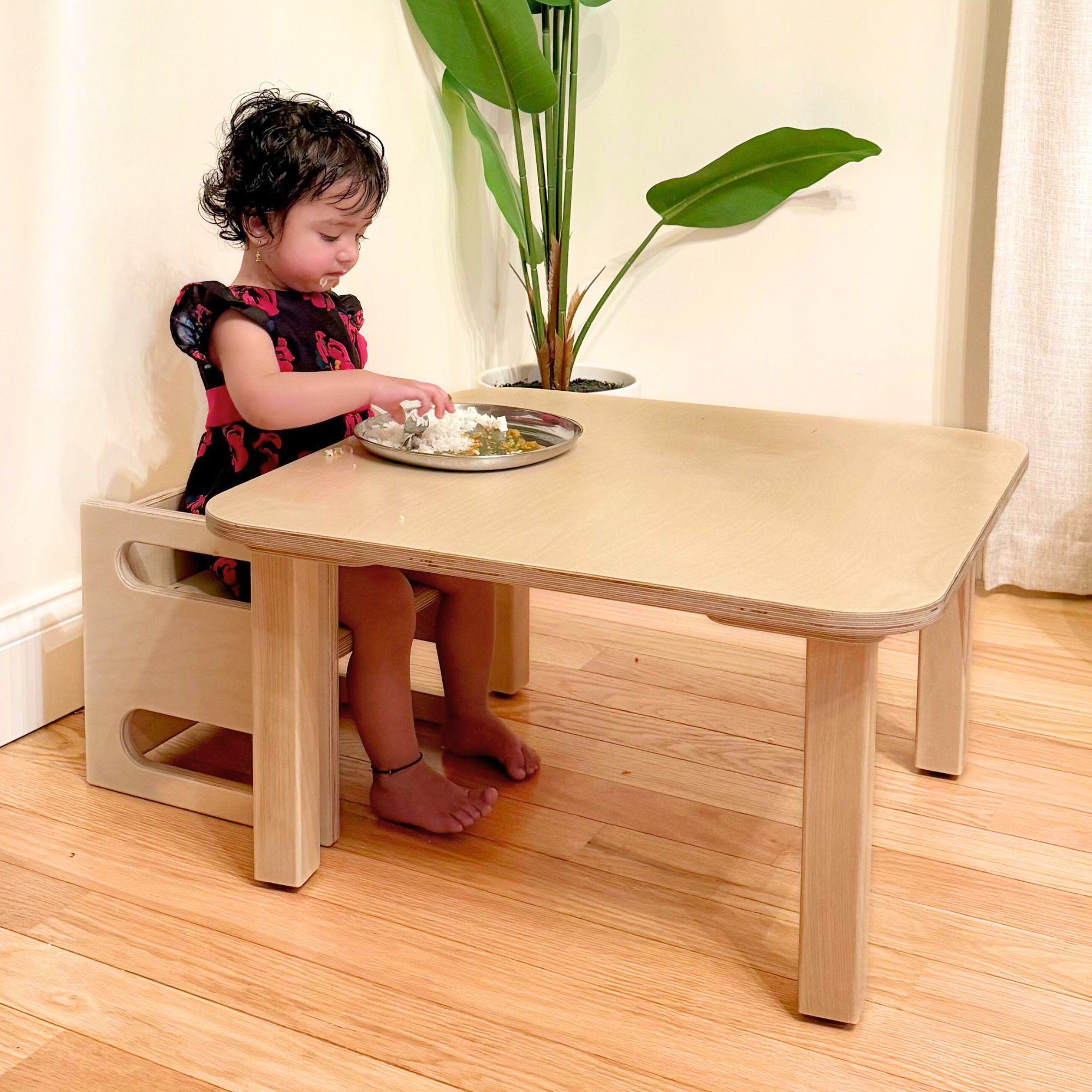 Child sitting at a small wooden table with a chair, playing with a toy.
