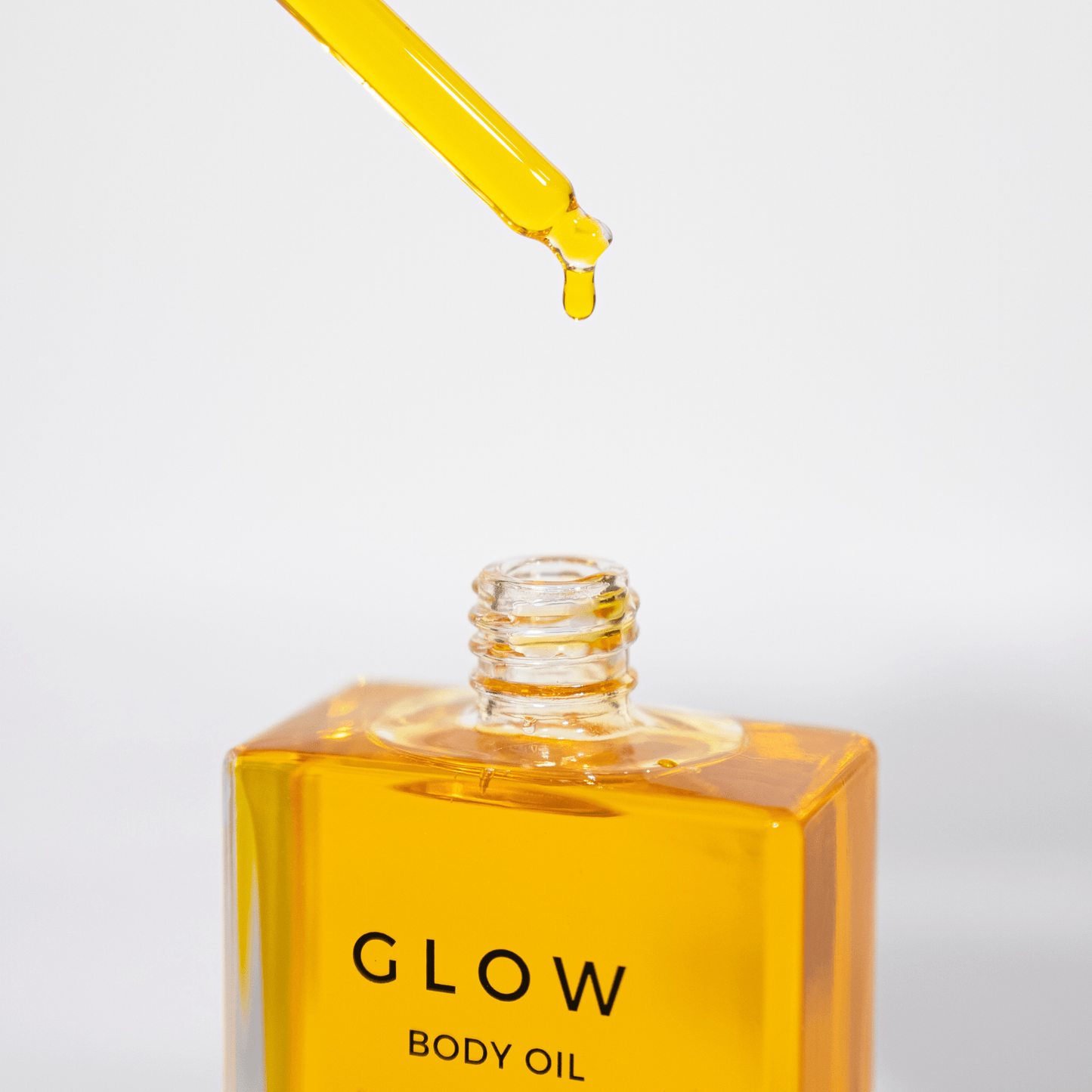 Yellow body oil with dropper labeled 'GLOW' on a white background