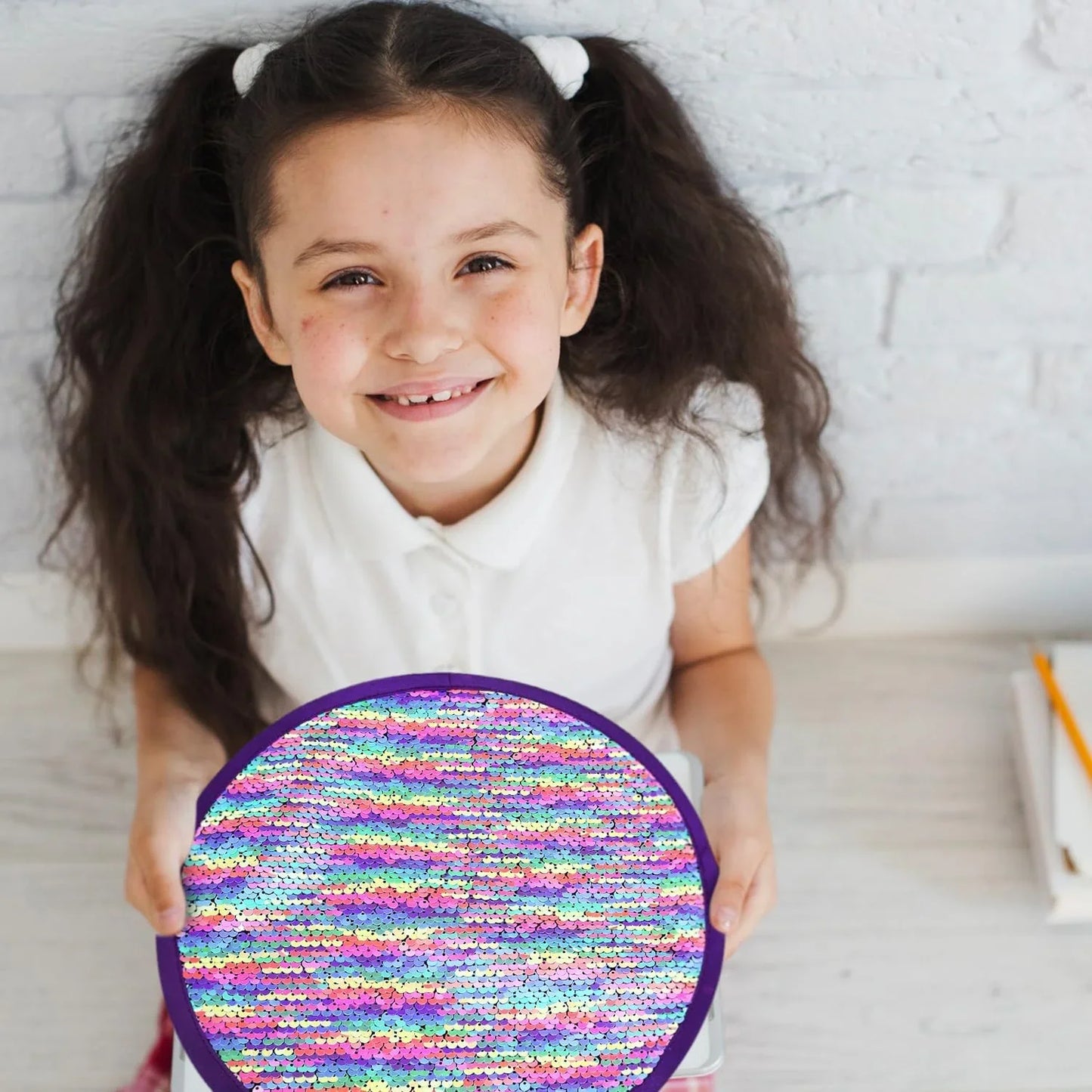 Smiling girl holding a round rainbow sequin sensory toy for kids
