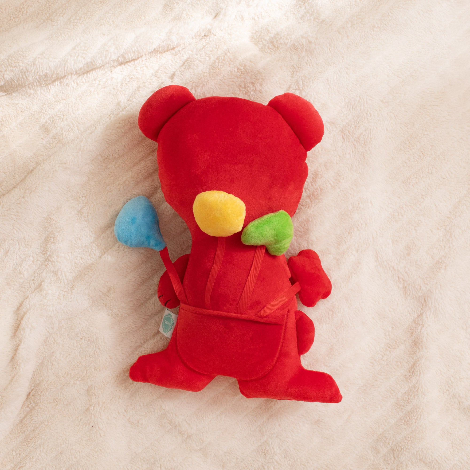 Red plush toy with colorful bow on a beige blanket