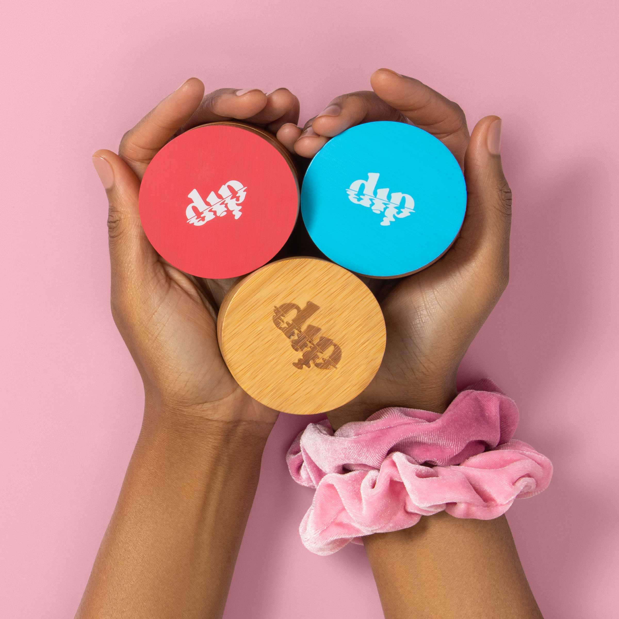 Two hands holding three circular containers with 'dip' branding on a pink background