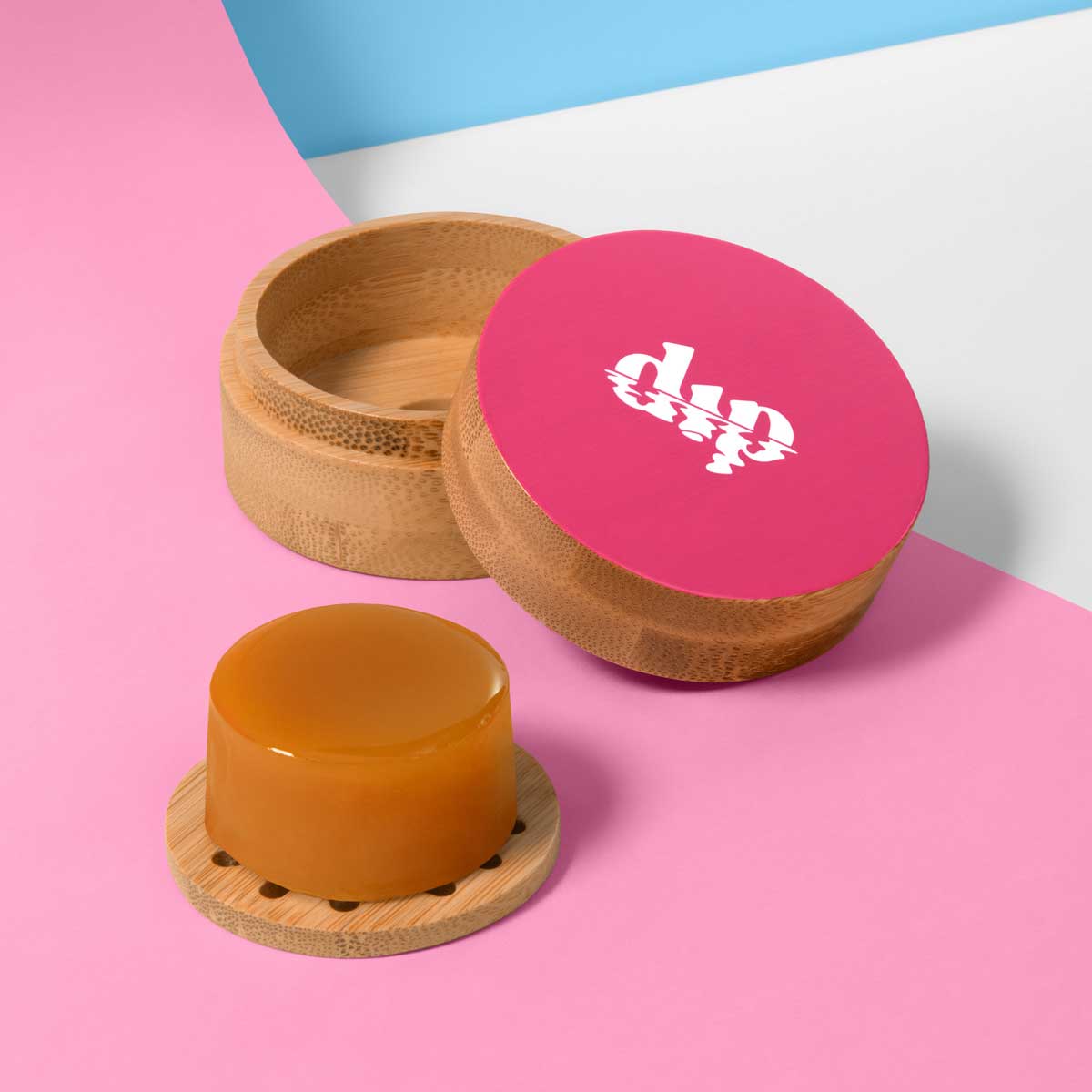 Bamboo container with pink lid featuring a logo, containing a yellowish product on a colorful background.