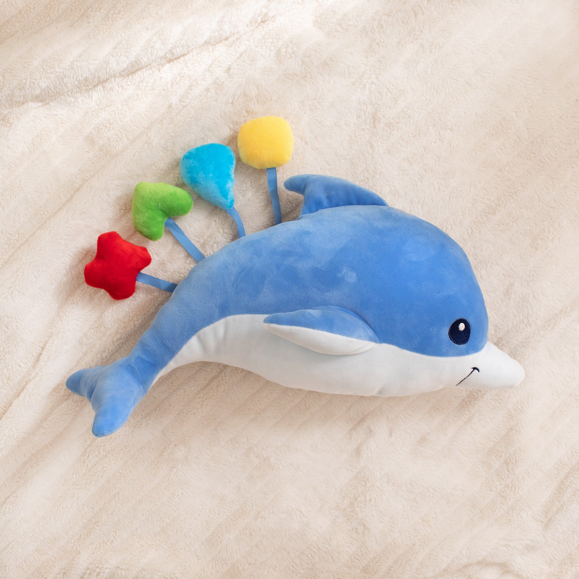 Blue dolphin plush toy with colorful flowers on a beige blanket