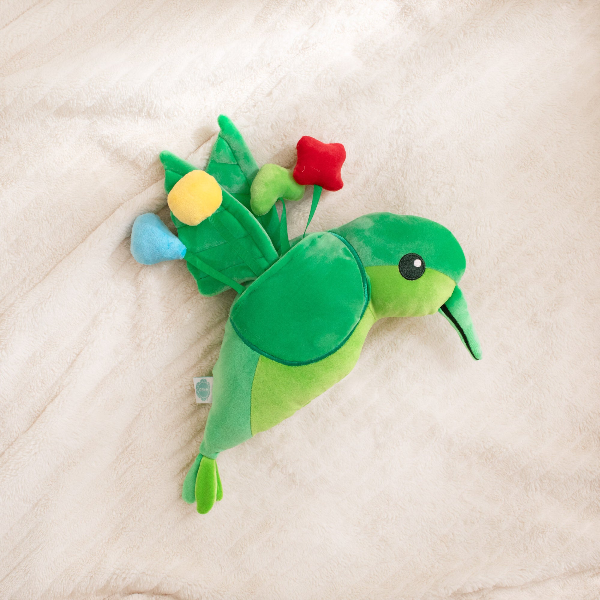 Green plush toy resembling a bird with colorful flowers on a beige surface