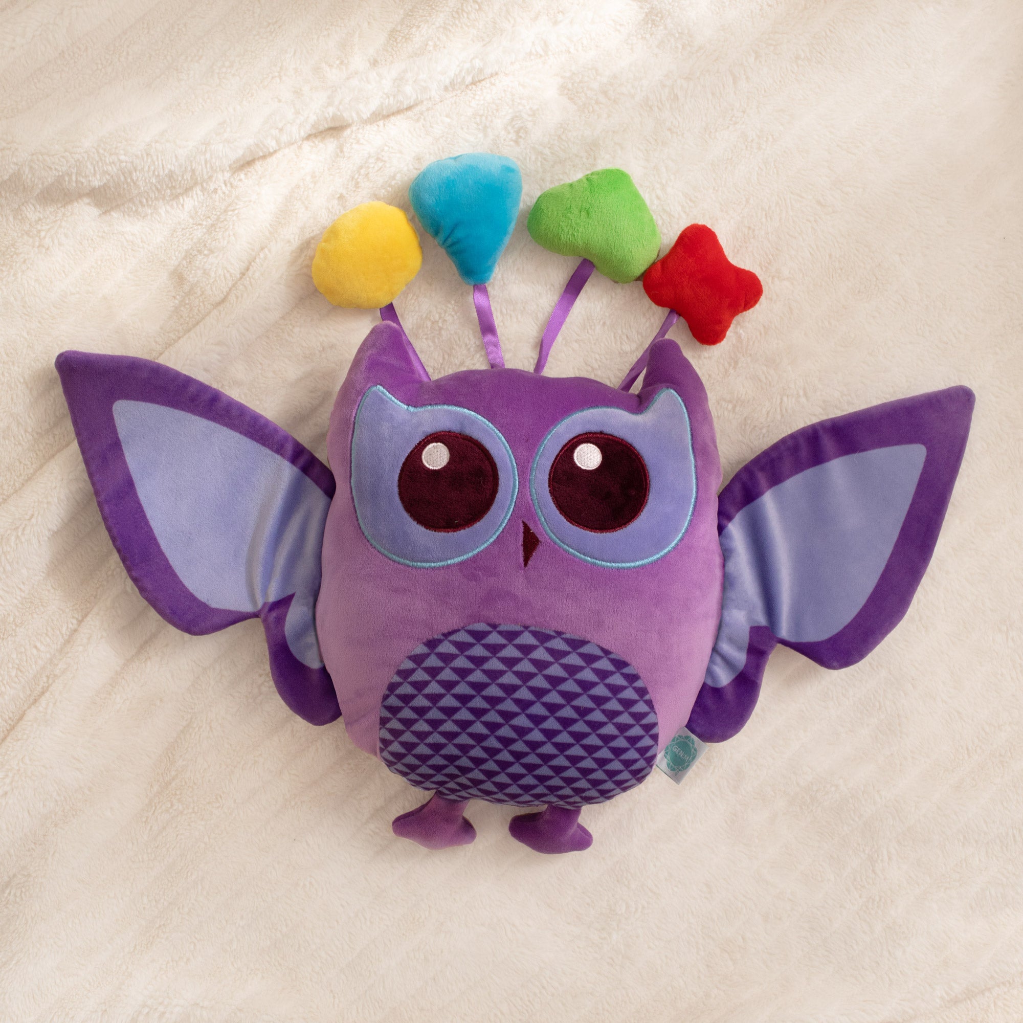 Purple owl plush toy with colorful pom-poms on a beige background