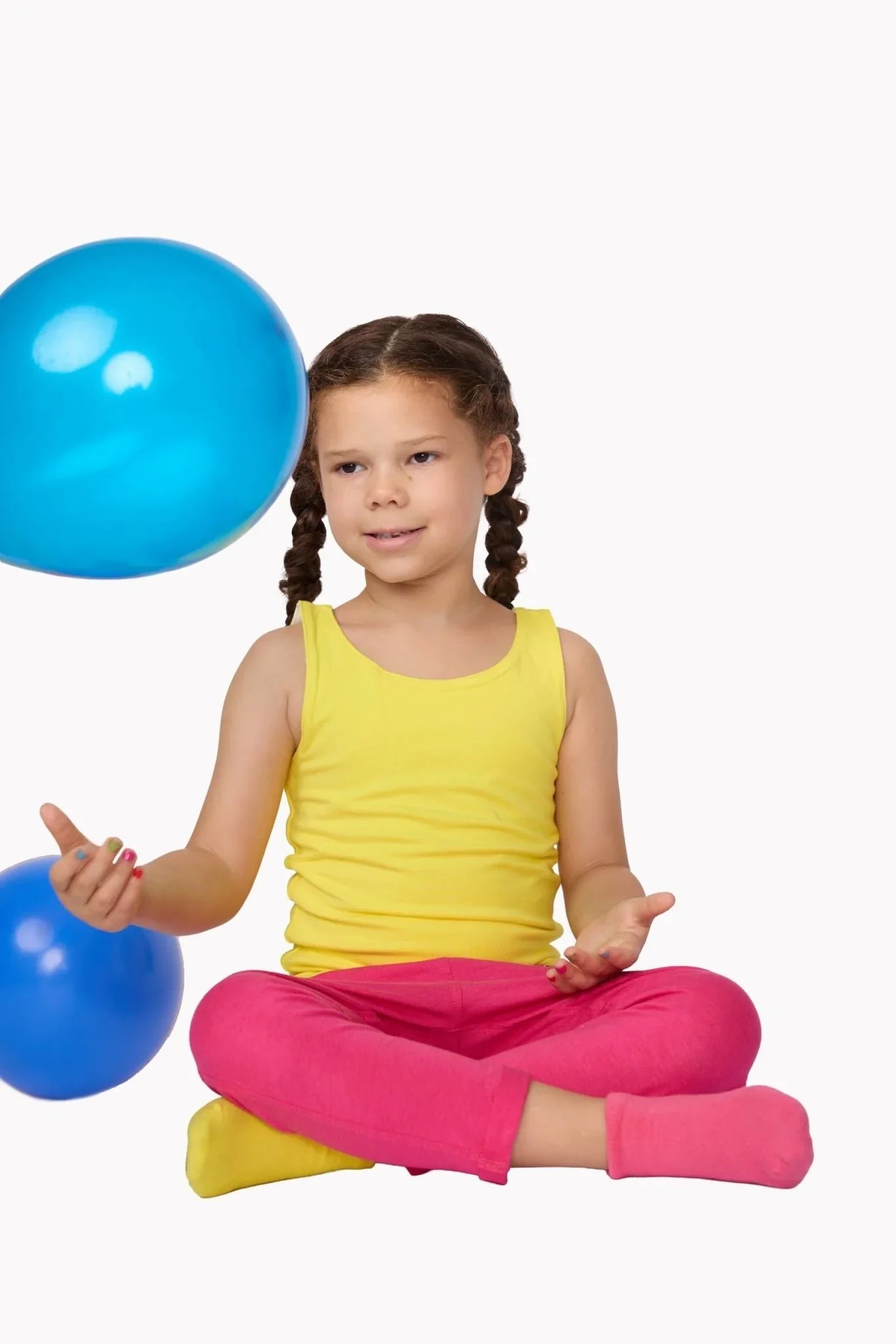 Child wearing sensory-friendly clothing sitting cross-legged, playing with blue balloons