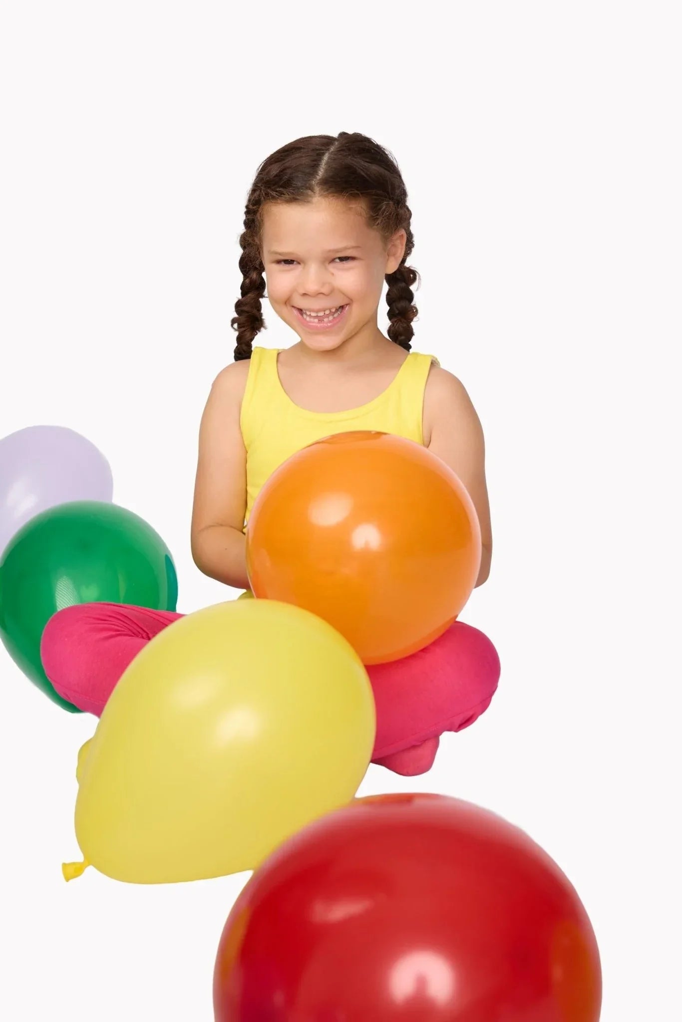 Smiling child with braids holding orange balloon, surrounded by colorful sensory-friendly balloons