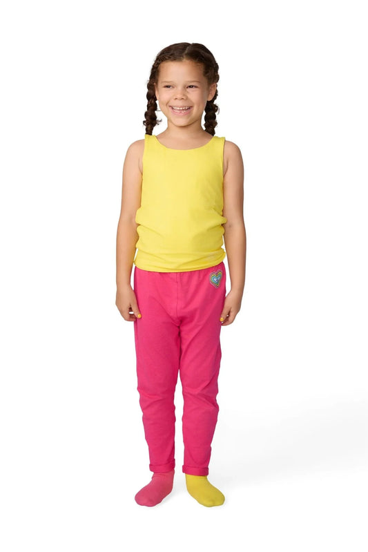 Smiling child wearing sensory-friendly yellow tank top and pink pants with heart patch.
