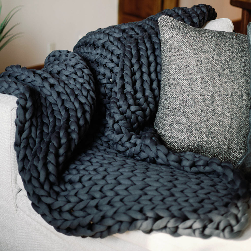 Cozy scene with a textured blue blanket draped over a white couch and a gray pillow.