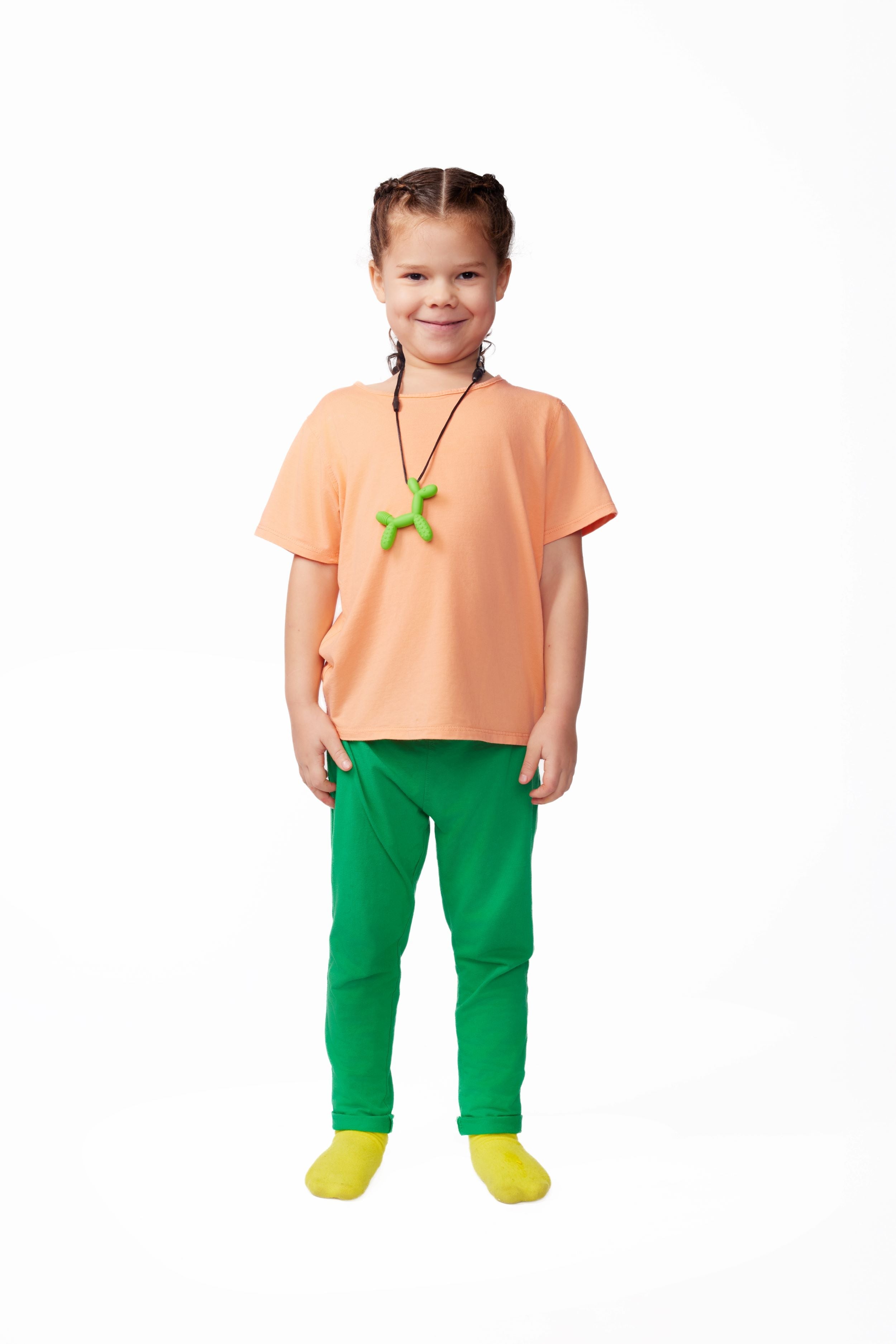 Child wearing an orange shirt, green pants, and yellow shoes on a white background