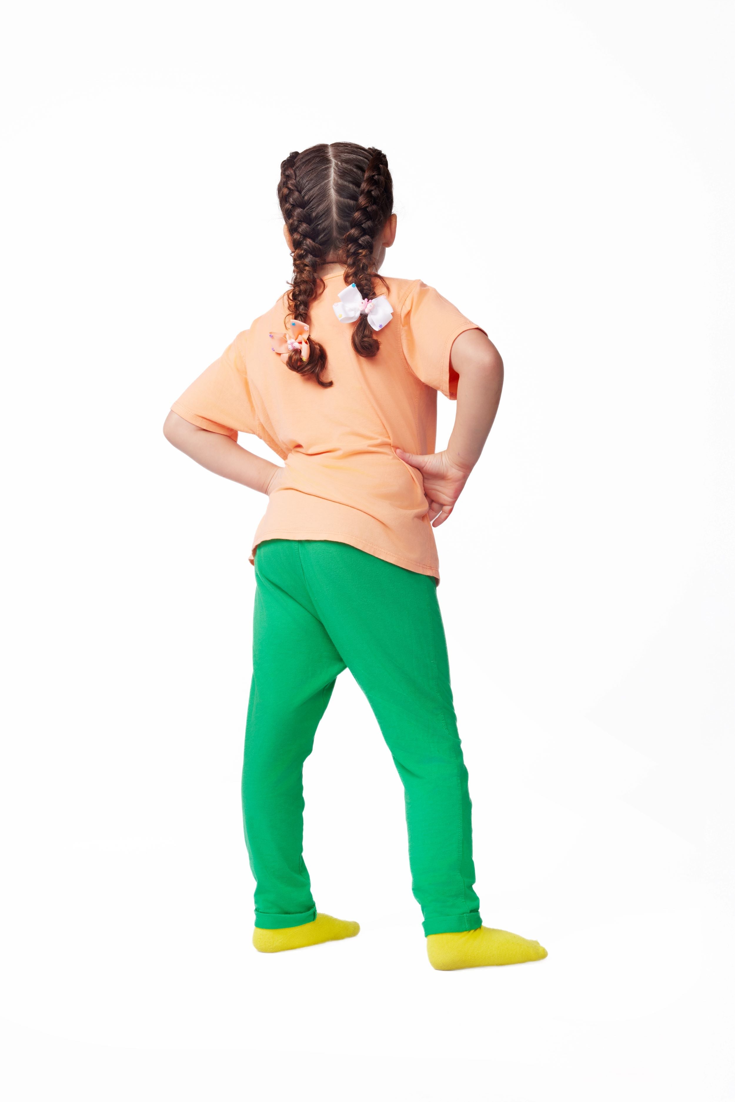 Person wearing a peach top and green pants on a white background
