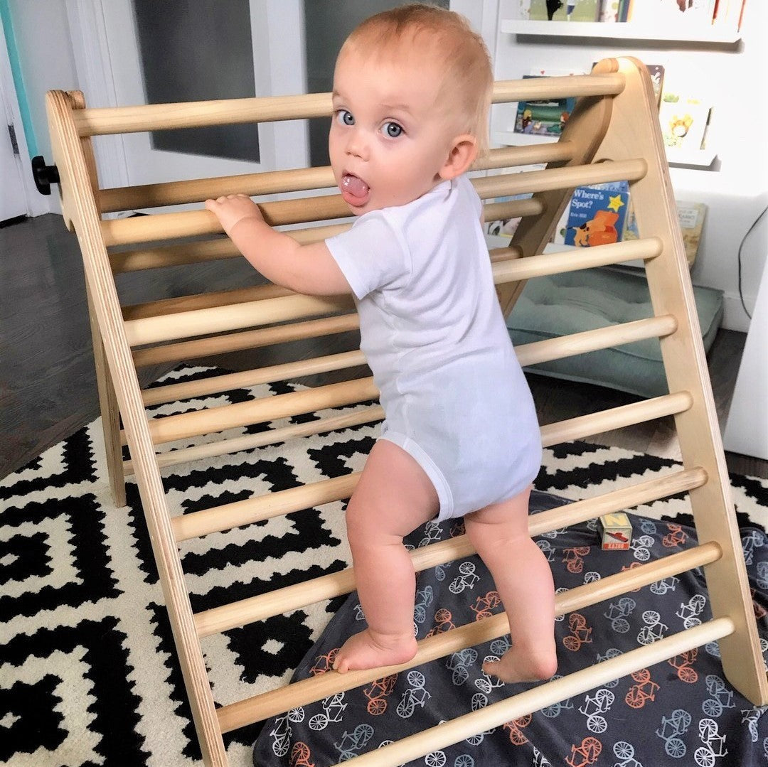 Baby climbing a wooden ladder on a patterned rug