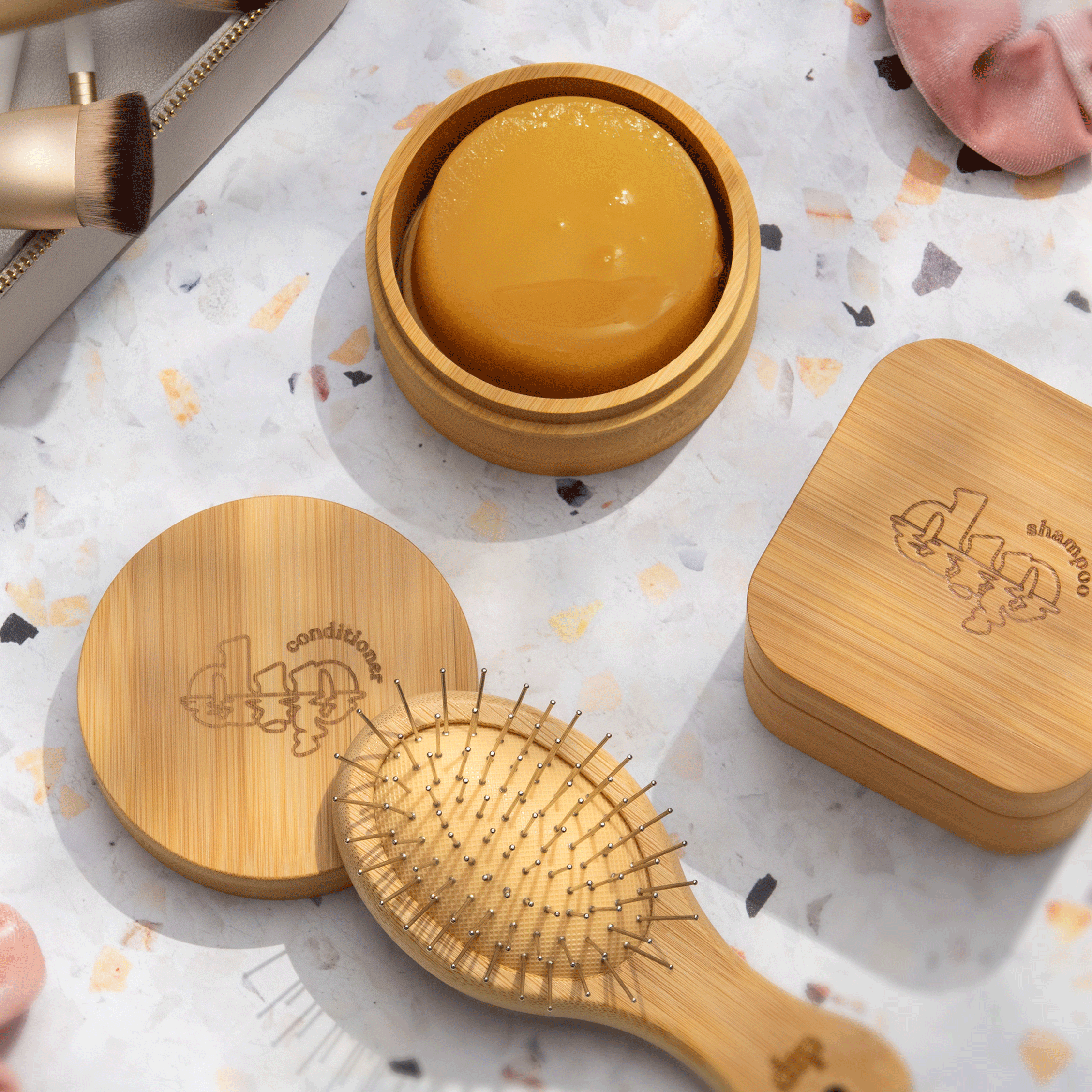 Bamboo hair care products including a brush, jar, and containers on a patterned surface.