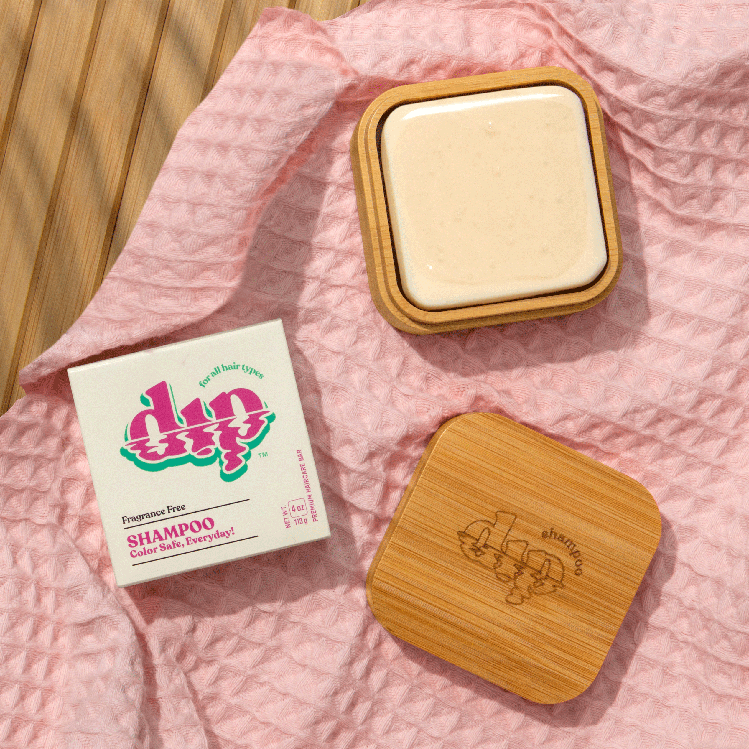 Bar of soap in a wooden container with 'dip' packaging on a pink fabric background