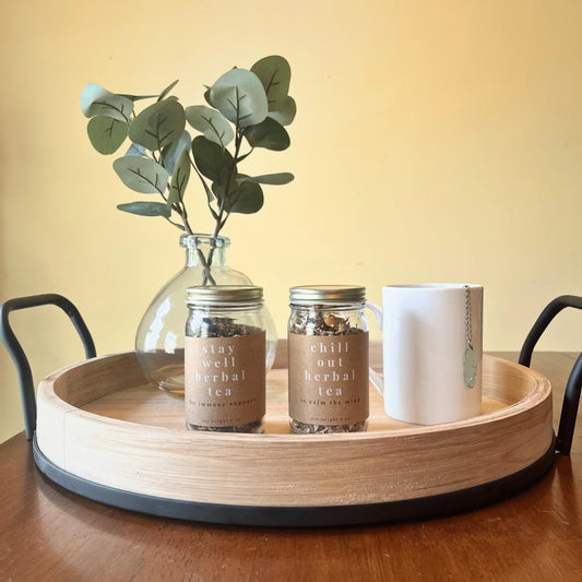 Jars of loose leaf herbal tea labeled 'stay well' and 'chill out' next to a mug on a wooden tray