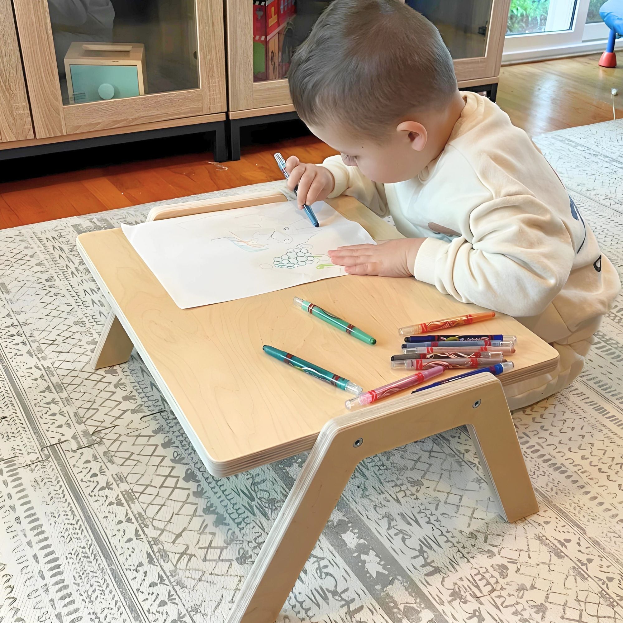 Child drawing on a small wooden table with colorful pens in a home setting.