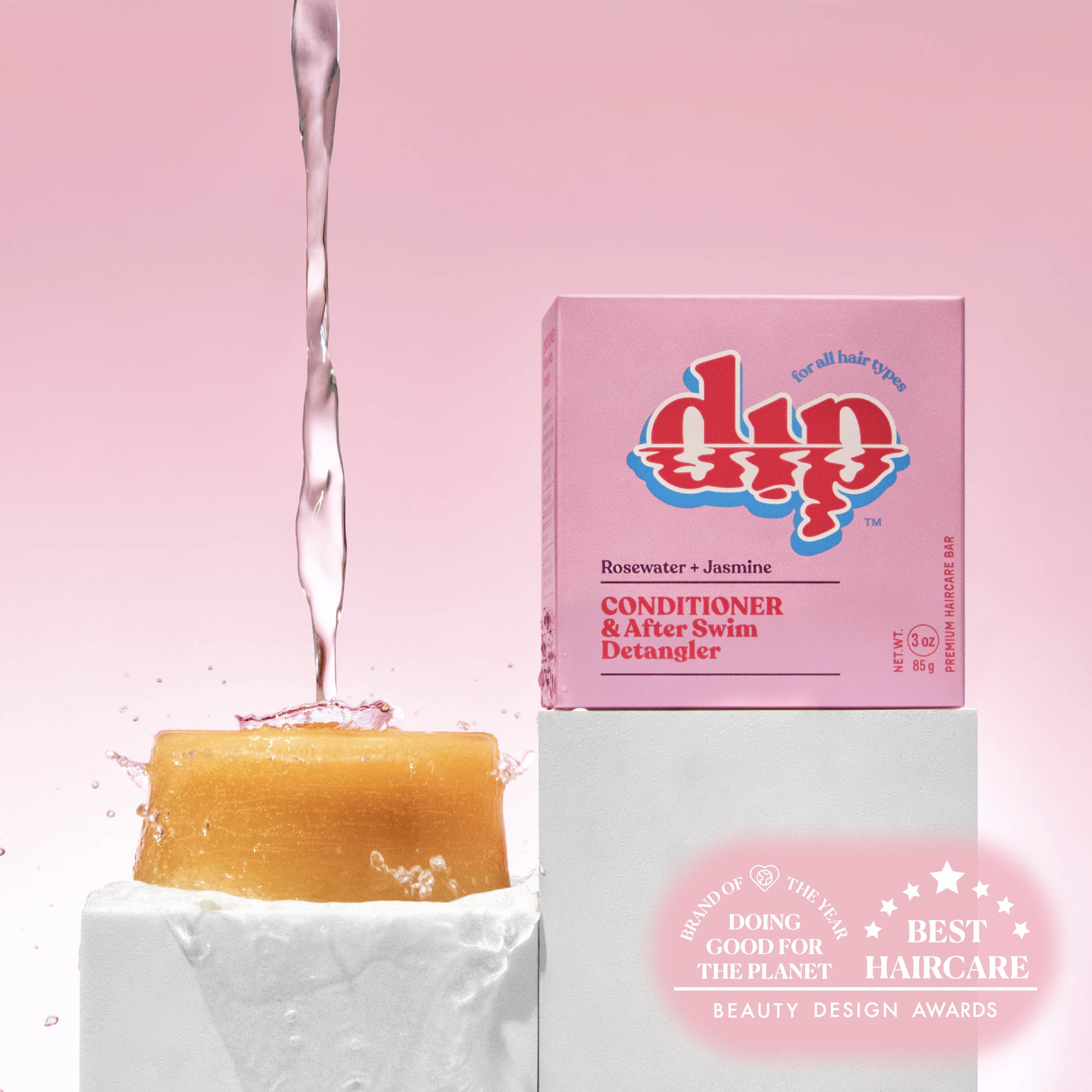 Dip soap with water being poured over it, next to its packaging on a pink background.