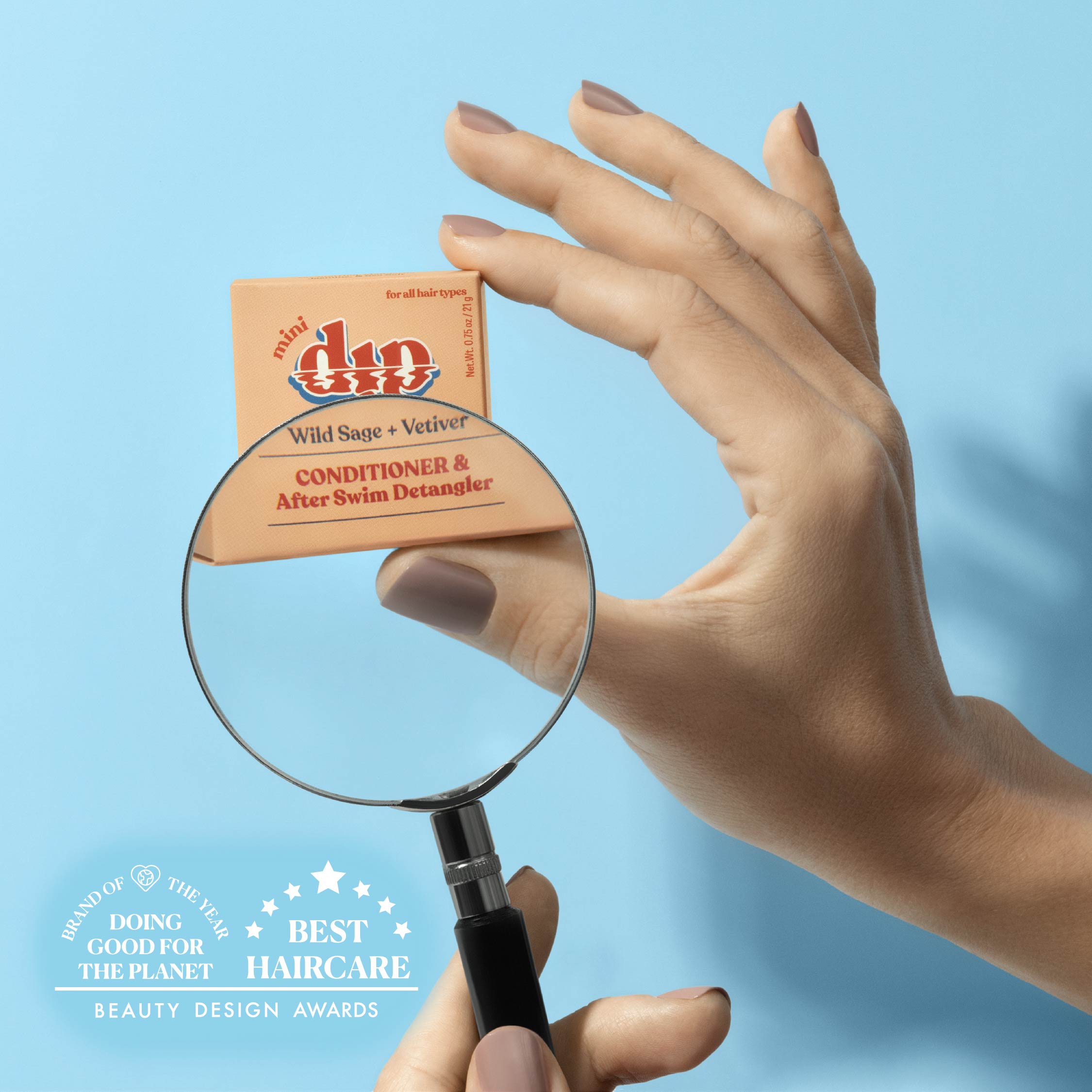 Hand holding a box of 'minidip' conditioner with a magnifying glass against a blue background