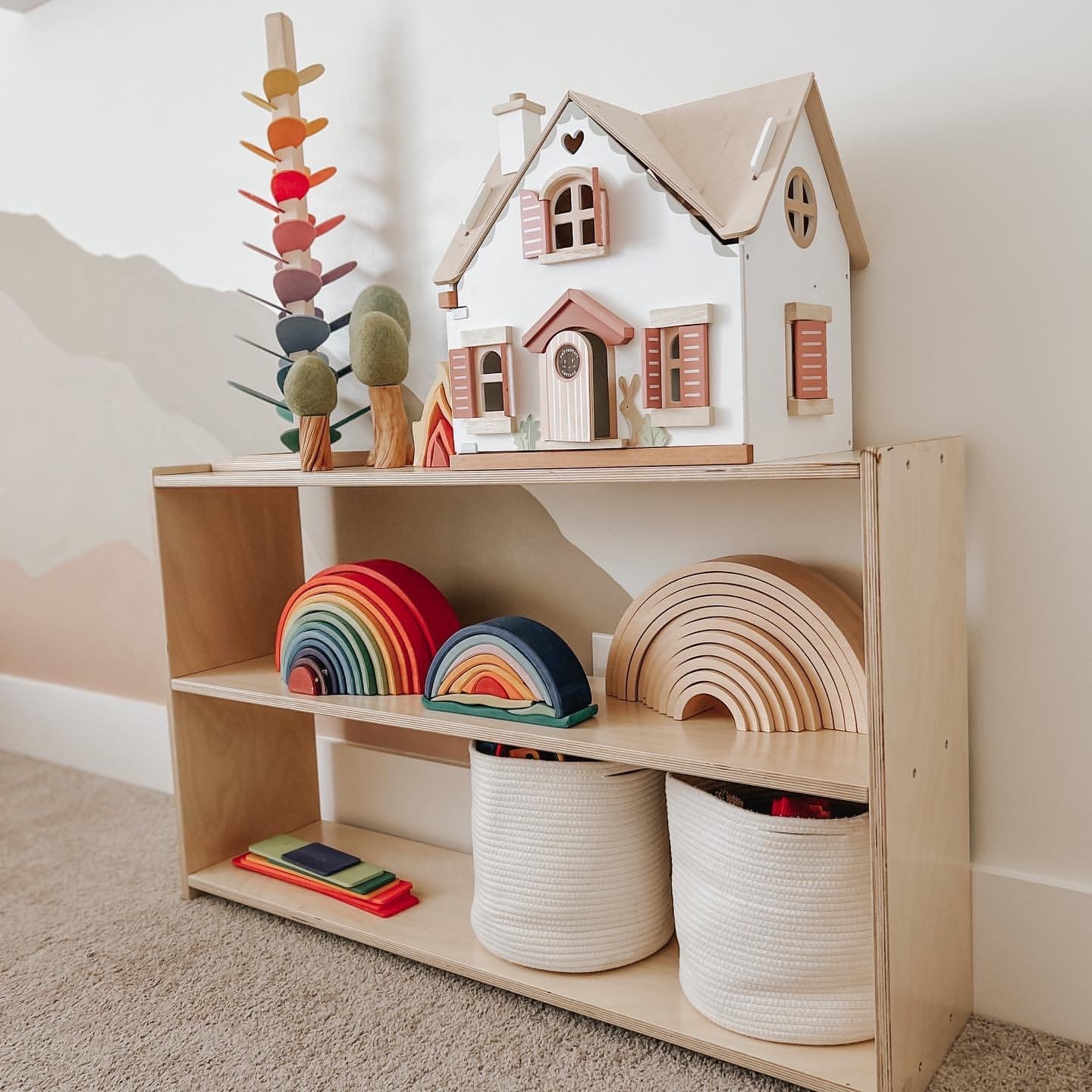 Wooden toy shelf with a dollhouse, rainbow toys, and storage baskets in a child's room.