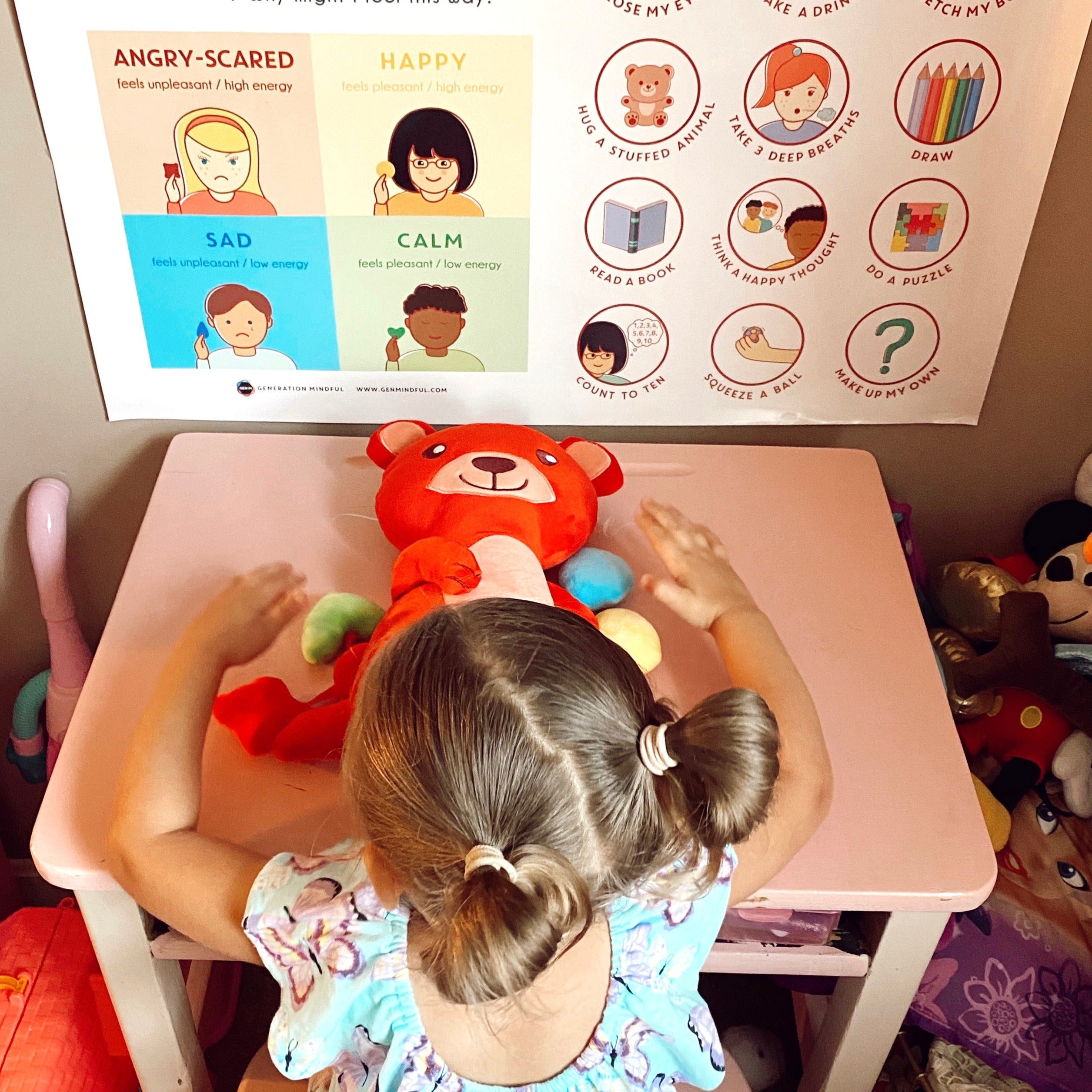 Child playing with a red teddy bear at a table with情绪管理 posters on the wall.