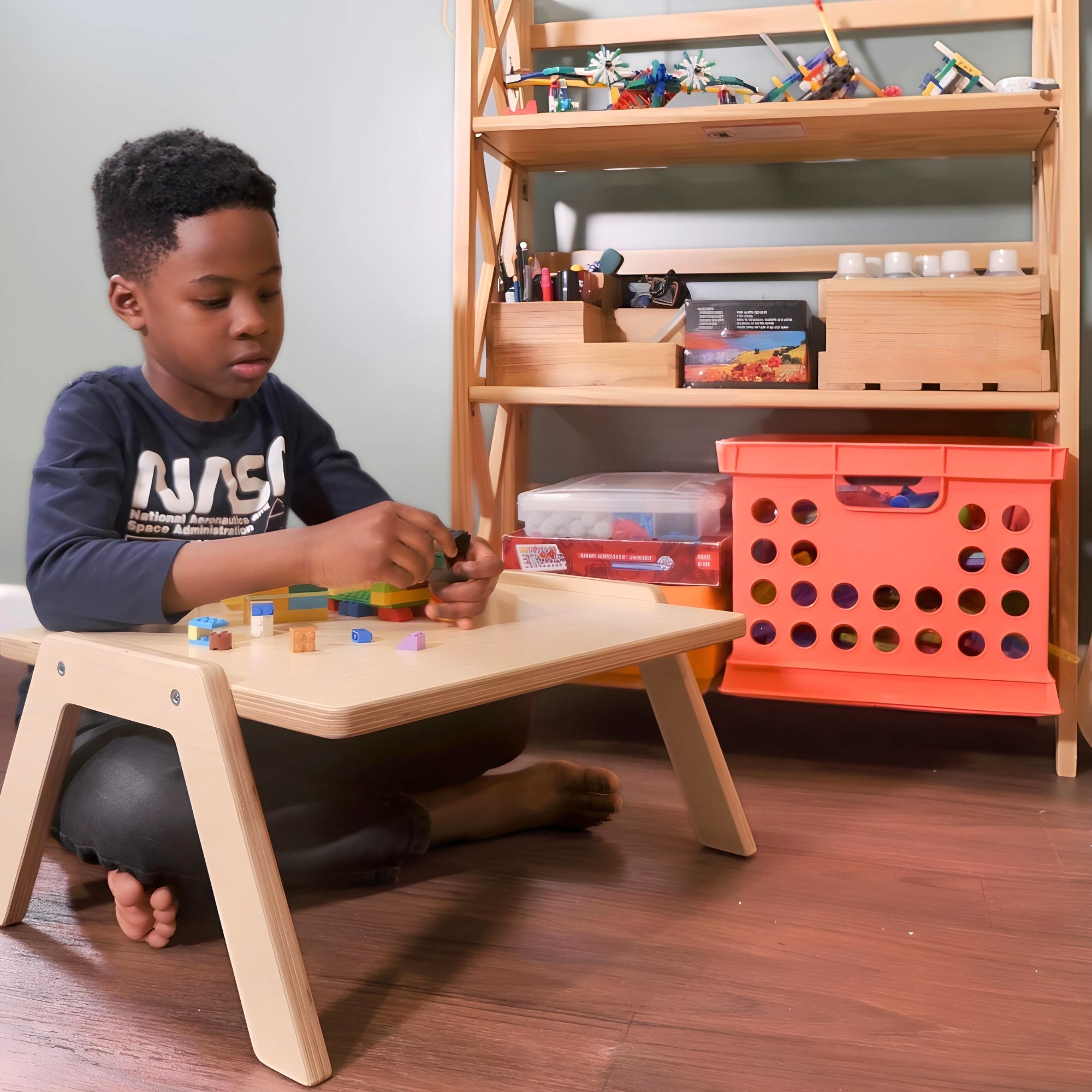 Child playing with toys at a wooden table in a room with shelves and storage bins.