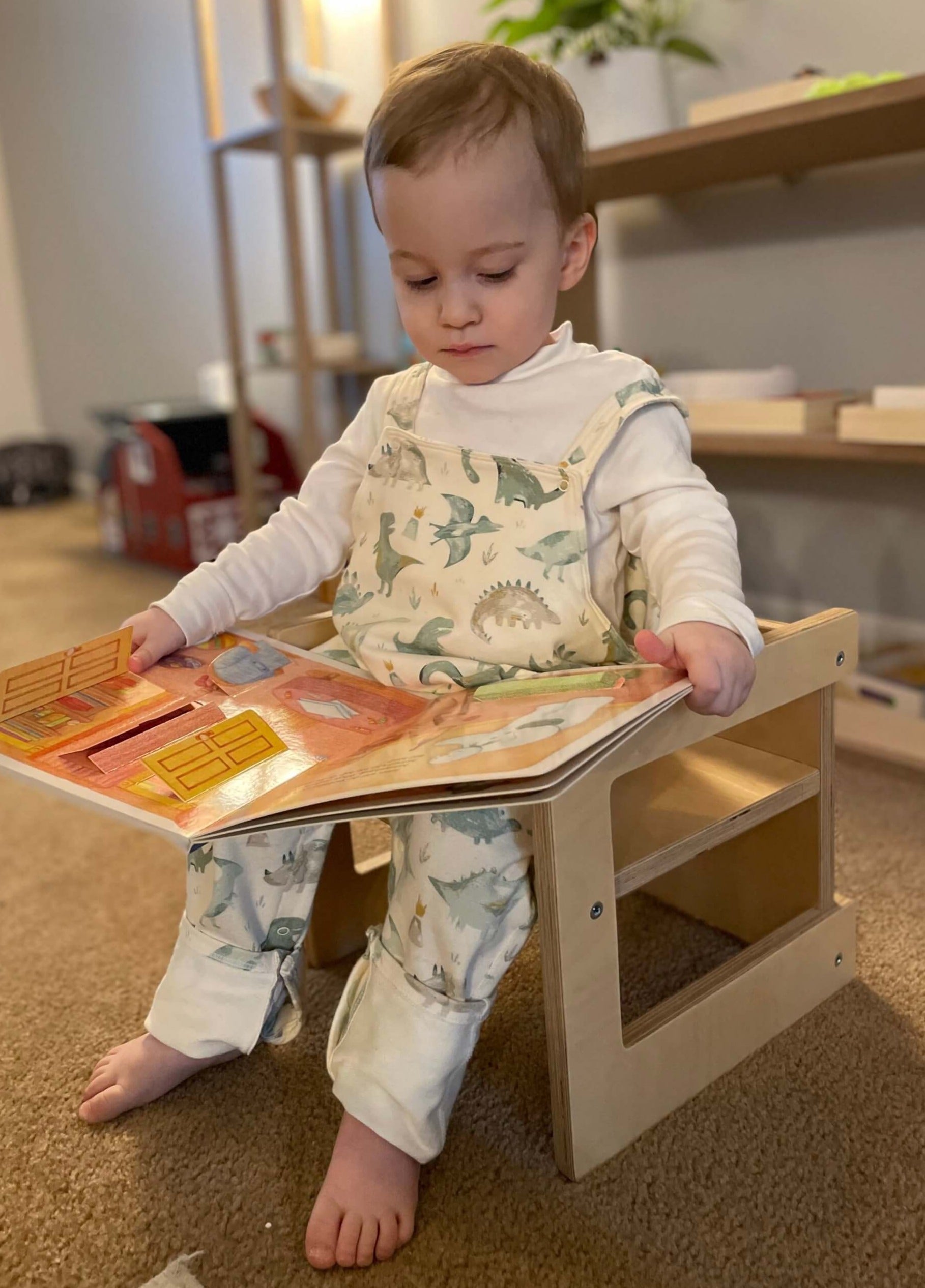 Child sitting on a wooden stool reading a colorful book indoors.