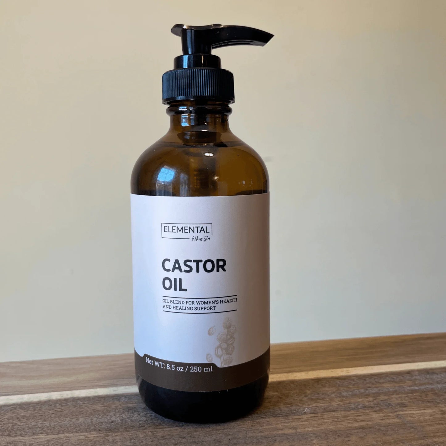 Amber pump bottle labeled castor oil, cold-pressed and hexane-free, on wood surface