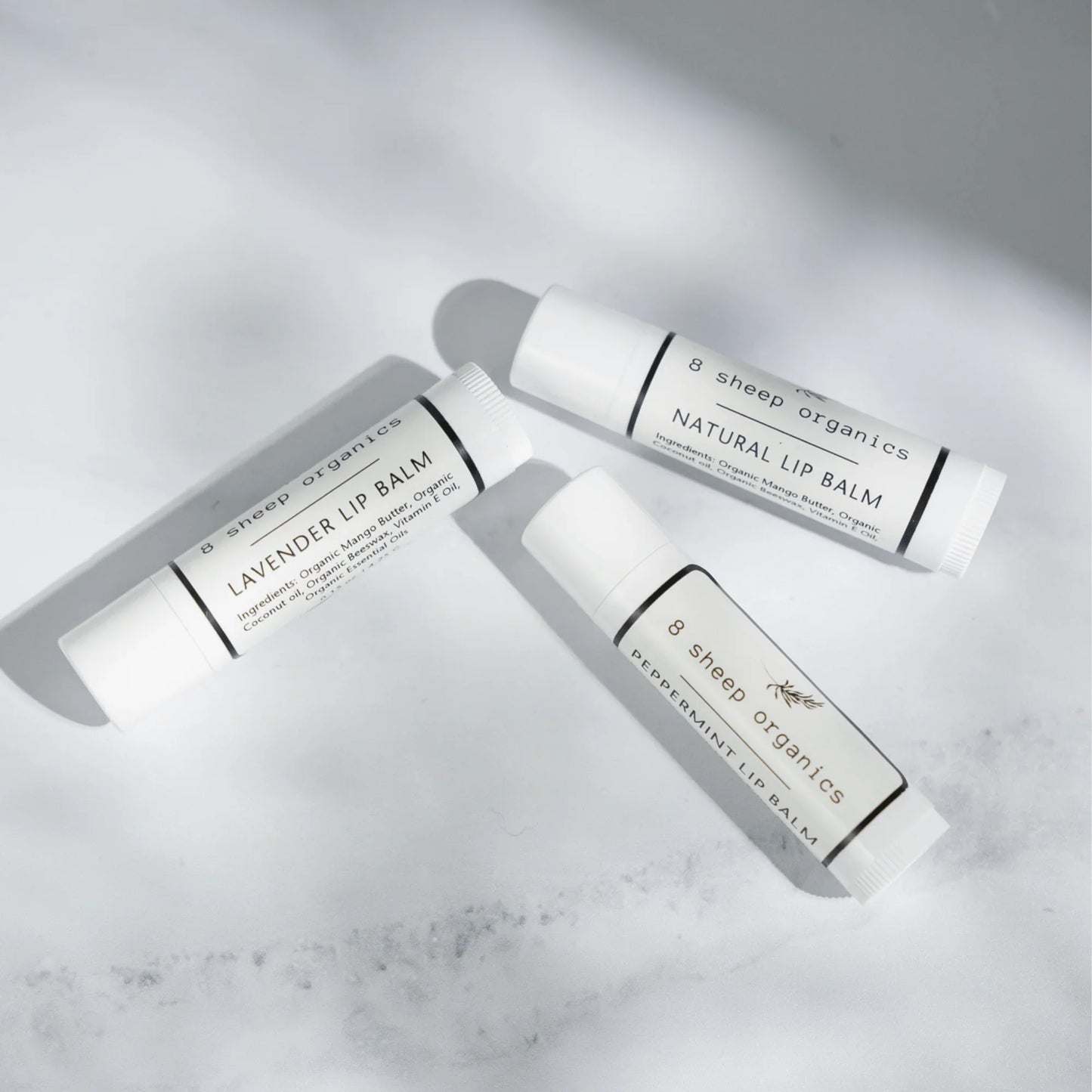 Three 8 Sheep Organics lip balm tubes—lavender, natural, and peppermint—on white surface.