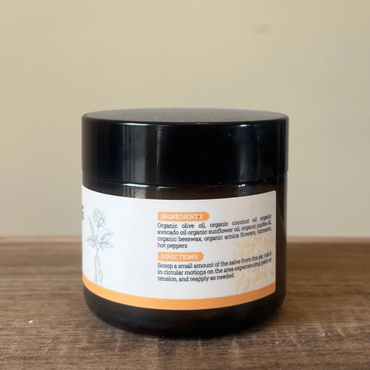 Round jar of warming botanical body balm with organic labeling styled next to fresh herbal ingredients.
