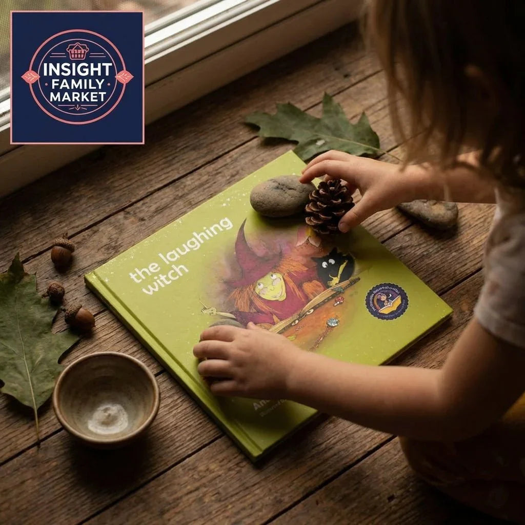 Child playing with pine cone and stones beside 'The Laughing Witch' children's book on wooden floor