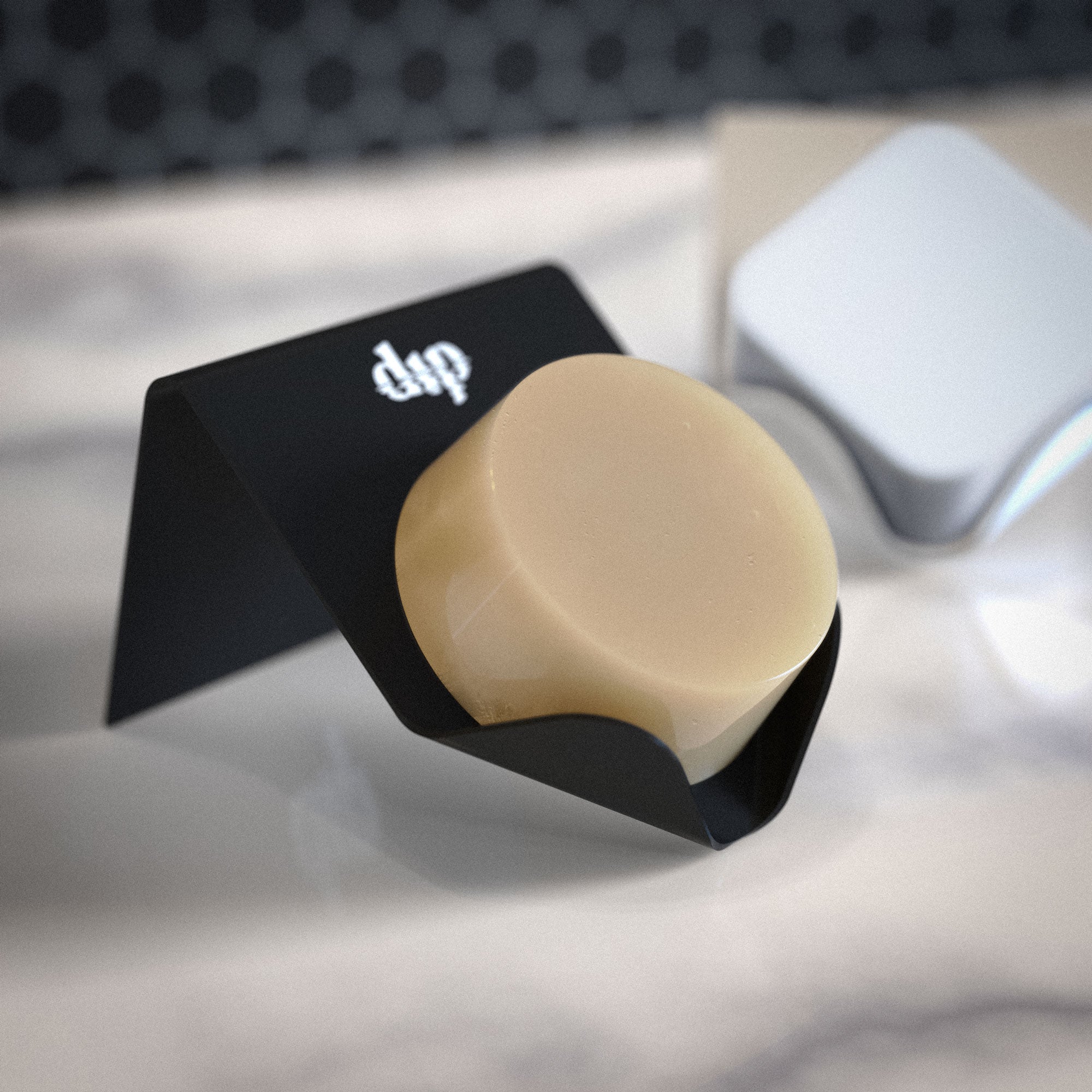 Beige soap bar on a black stand with 'dip' branding, blurred background