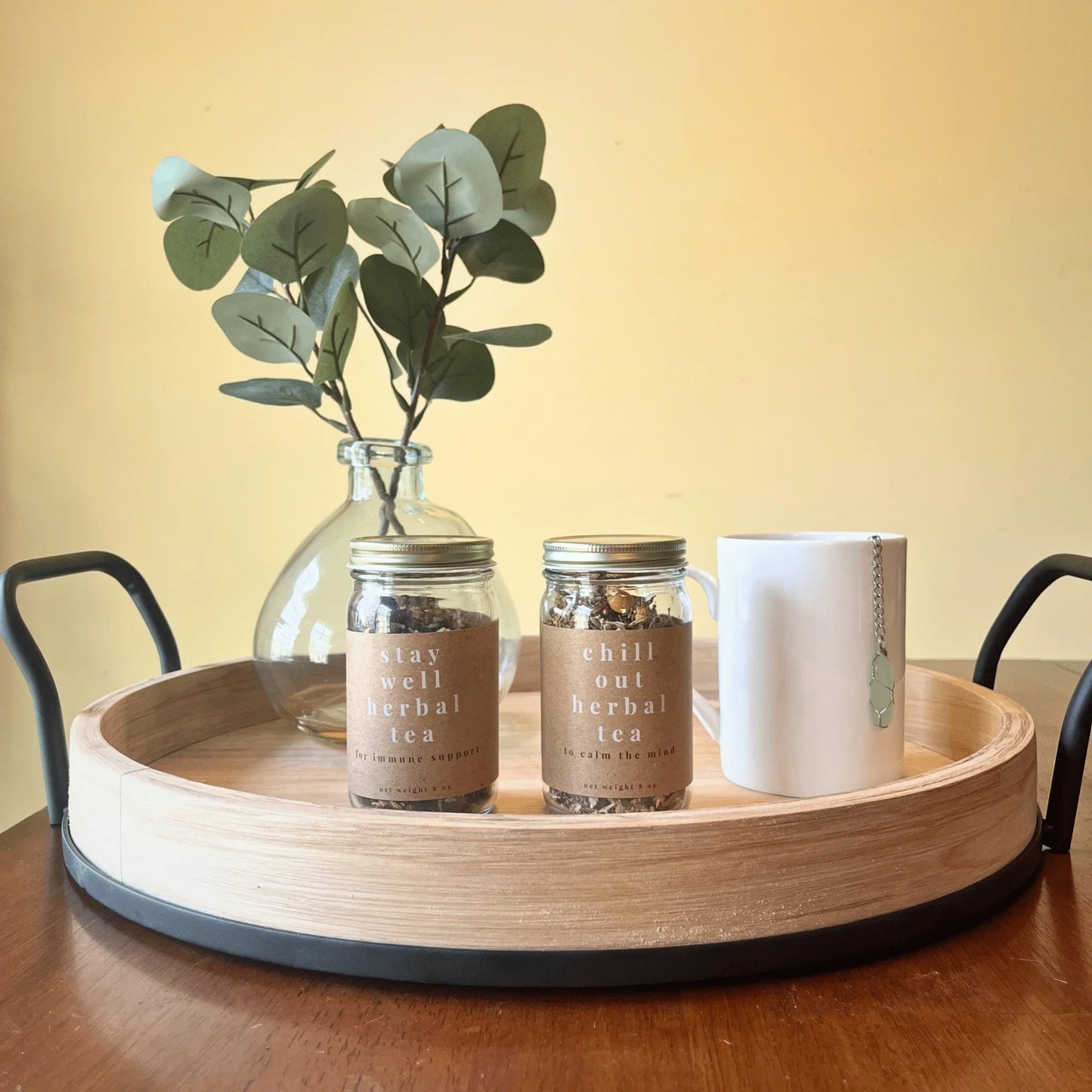 Loose leaf herbal tea jars, white mug, and vase with eucalyptus on wooden tray