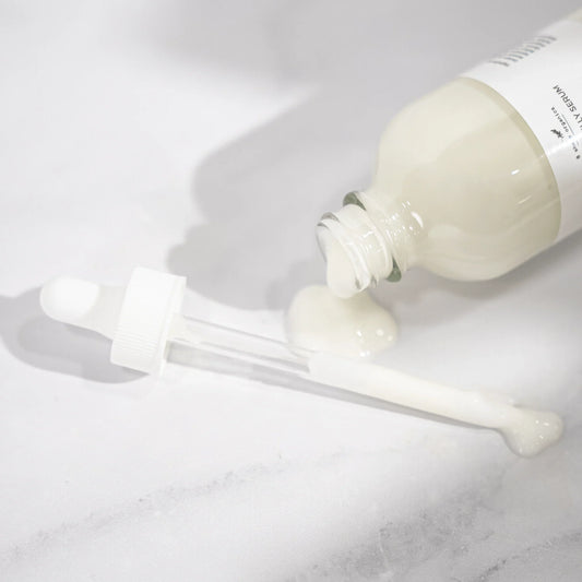 Spilled serum with dropper on white marble background, sensory skincare product
