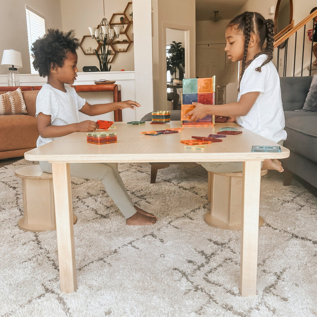 Two children playing with colorful blocks at a wooden table in a living room.