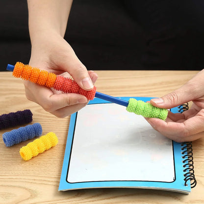 Hands placing colorful textured sensory pencil grips on a blue pencil next to a notepad.
