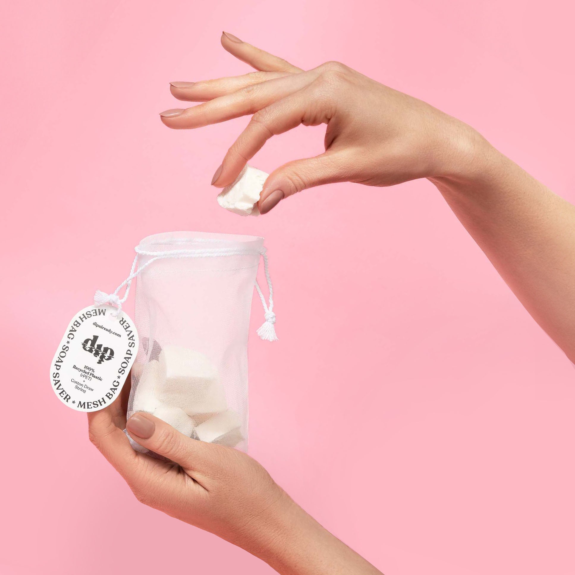 Hand holding a small bag of cotton pads with a pink background