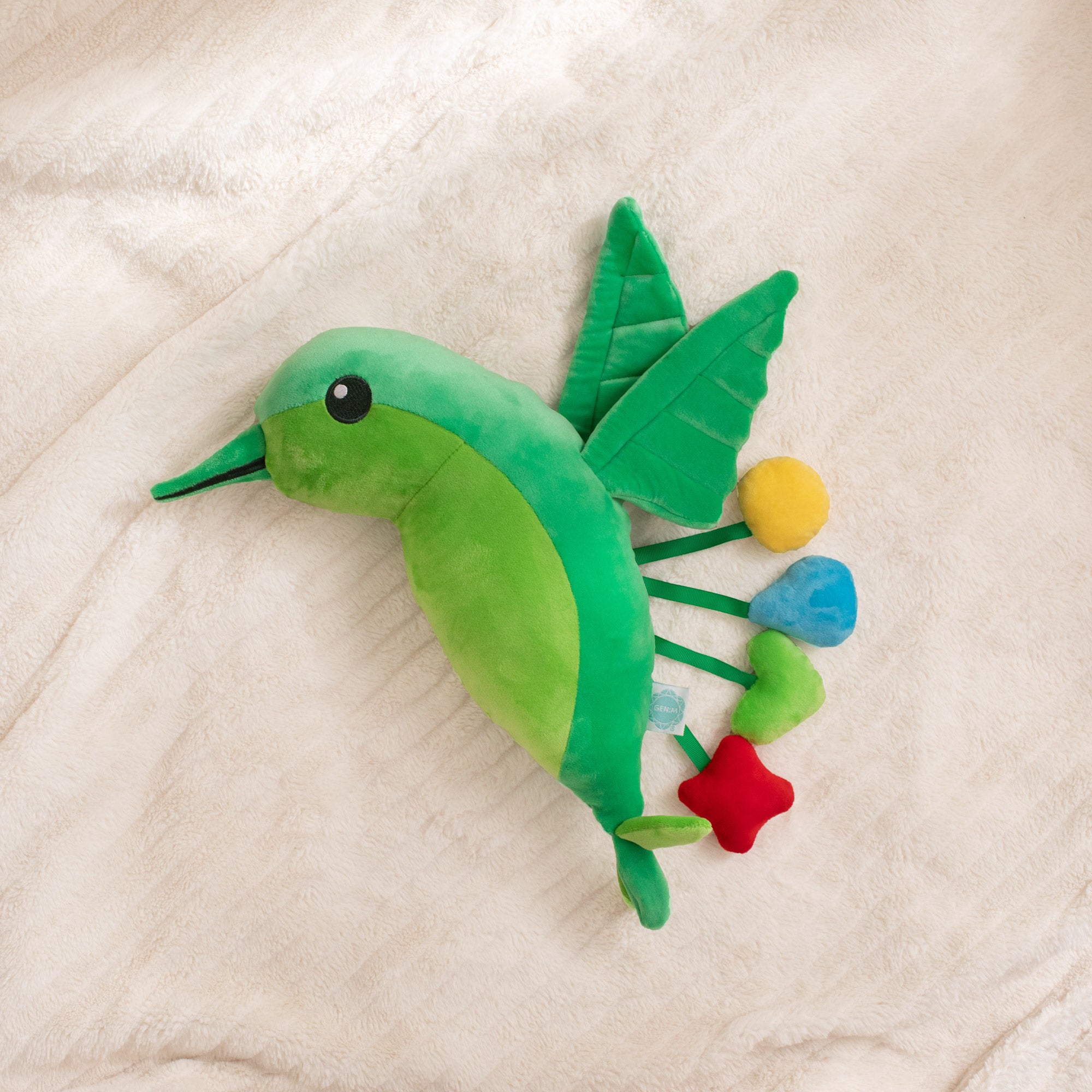 Green plush toy resembling a fish with colorful flowers on a beige blanket