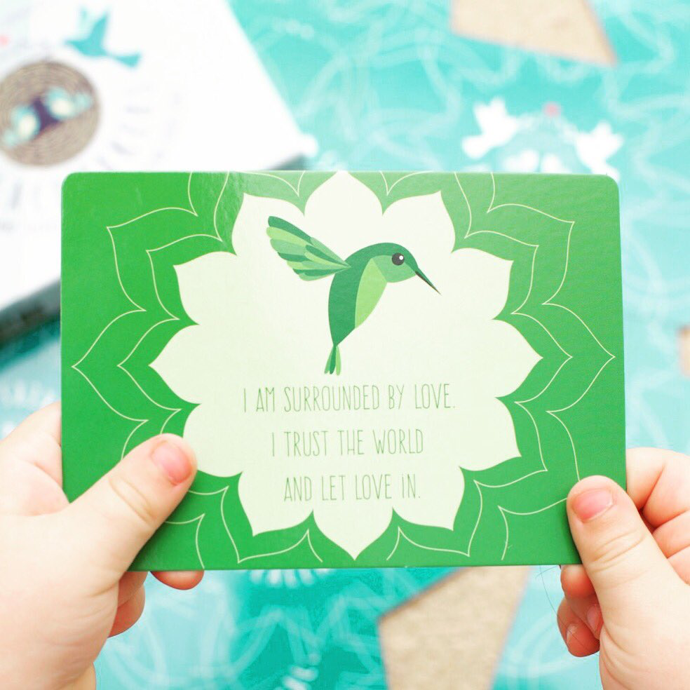 Green card with a hummingbird design and motivational text held by hands against a blurred background