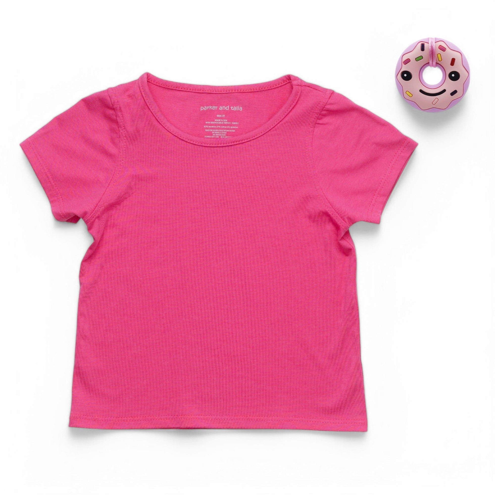 Pink t-shirt on a white background with a pink donut-shaped object next to it.