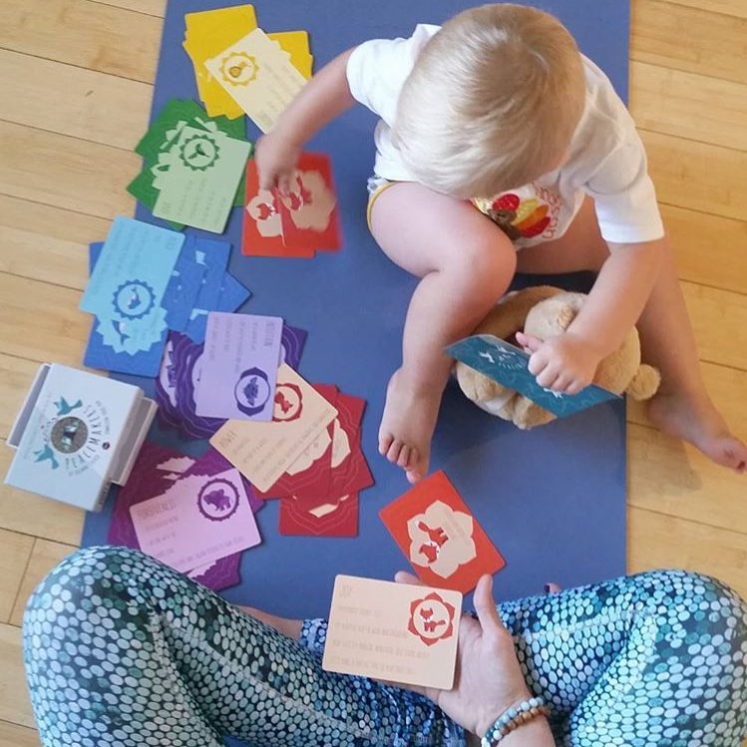Child playing with colorful cards on a blue mat, supervised by an adult.