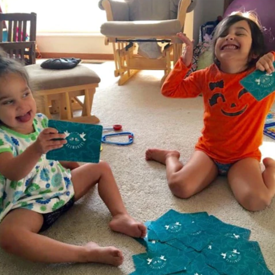 Two children playing with blue cards on a carpeted floor.