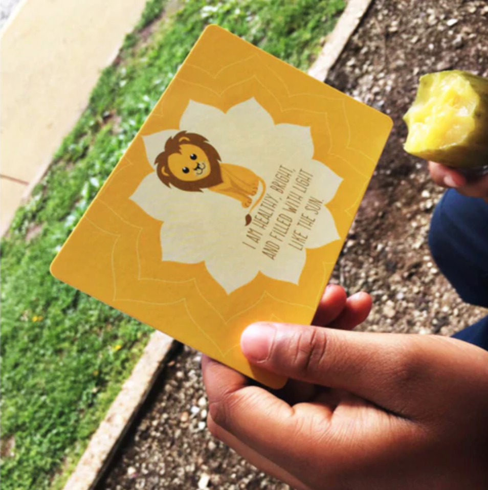 Hand holding a yellow card with a lion illustration and text, outdoors.