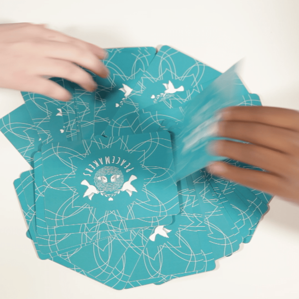 Teal paper with white patterns being folded by hands on a white background