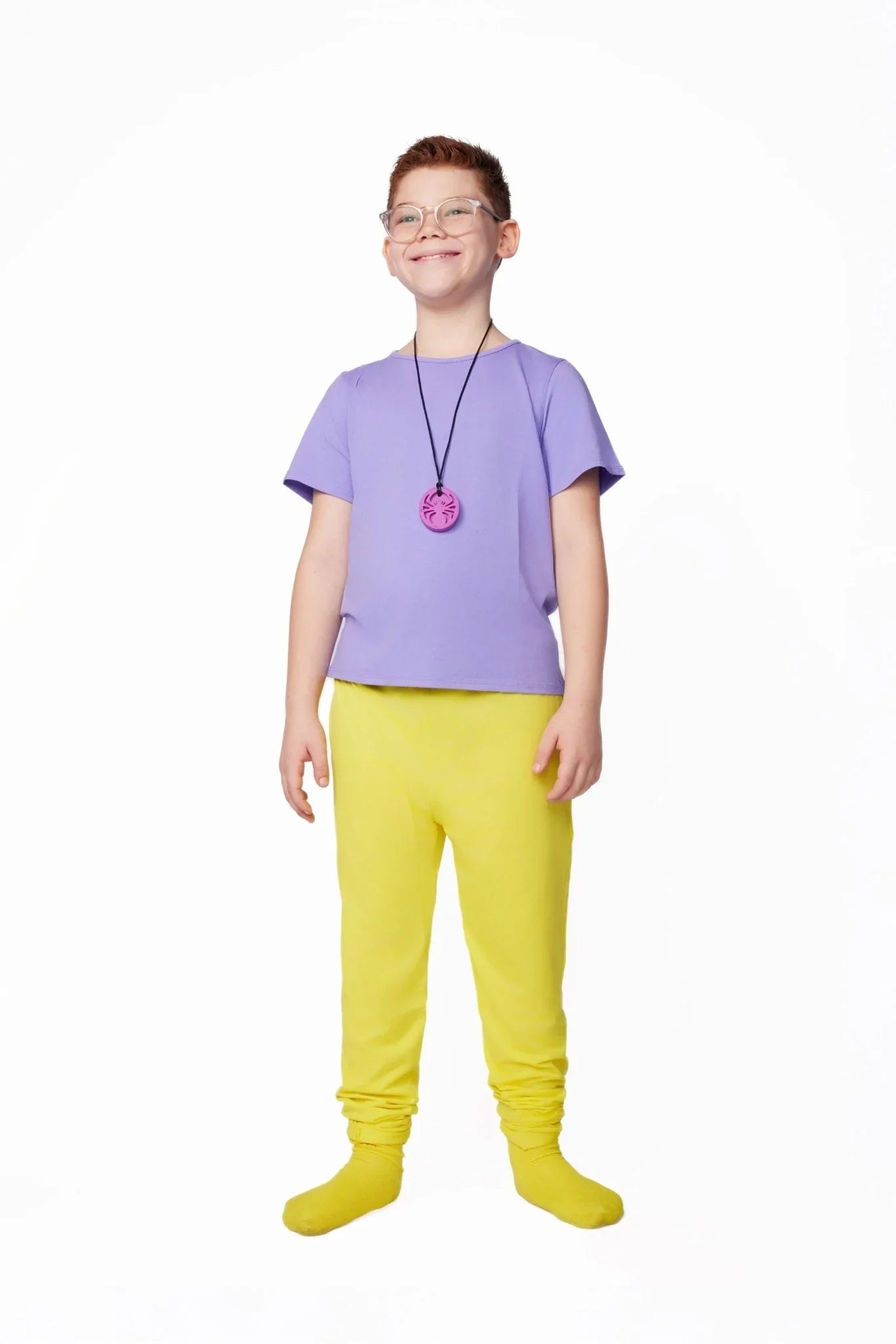 Child wearing sensory-friendly purple shirt, yellow pants, and pink chewable necklace