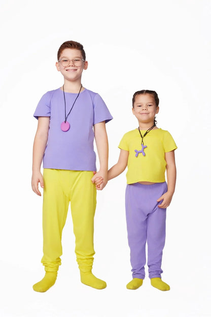 Two children in sensory-friendly clothing, holding hands, wearing colorful chewable necklaces.