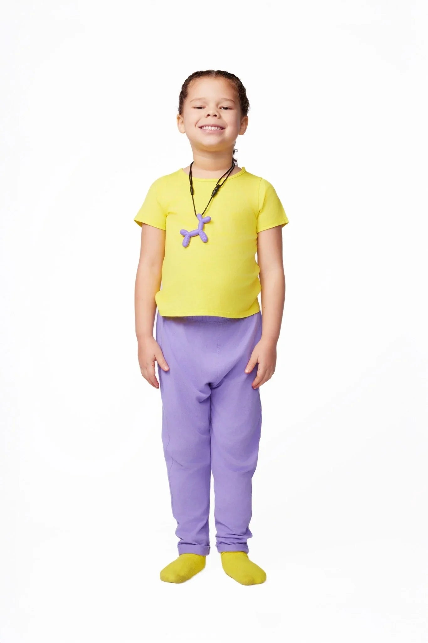 Smiling child in sensory-friendly yellow shirt, purple pants, and a purple chew necklace.