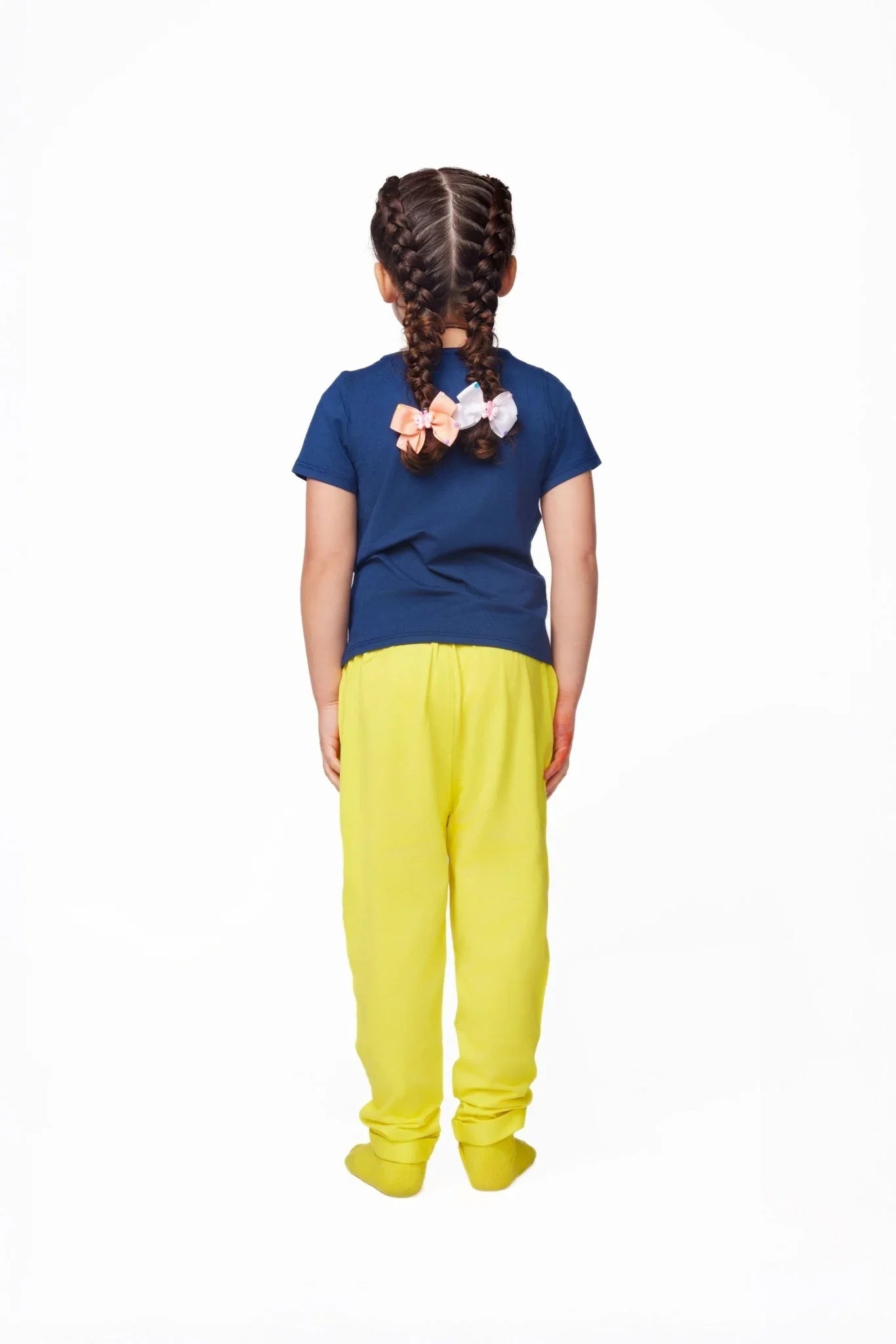 Child with braided hair and bows wearing a blue shirt and yellow sensory-friendly pants