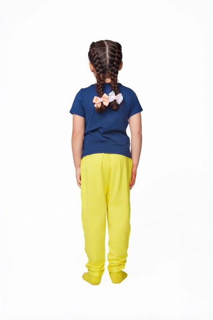 Child in blue sensory-friendly shirt and yellow pants, braided hair, back view